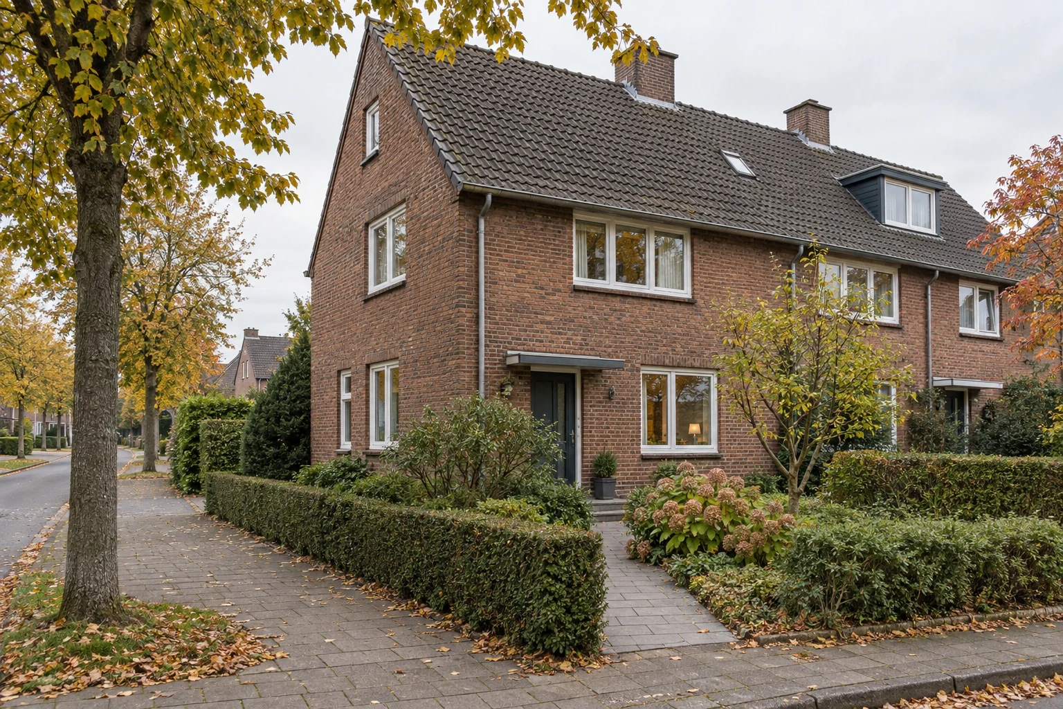 Backsteinhaus mit schmalem Vorgarten und reifen Bäumen in einer ruhigen Wohnstraße.